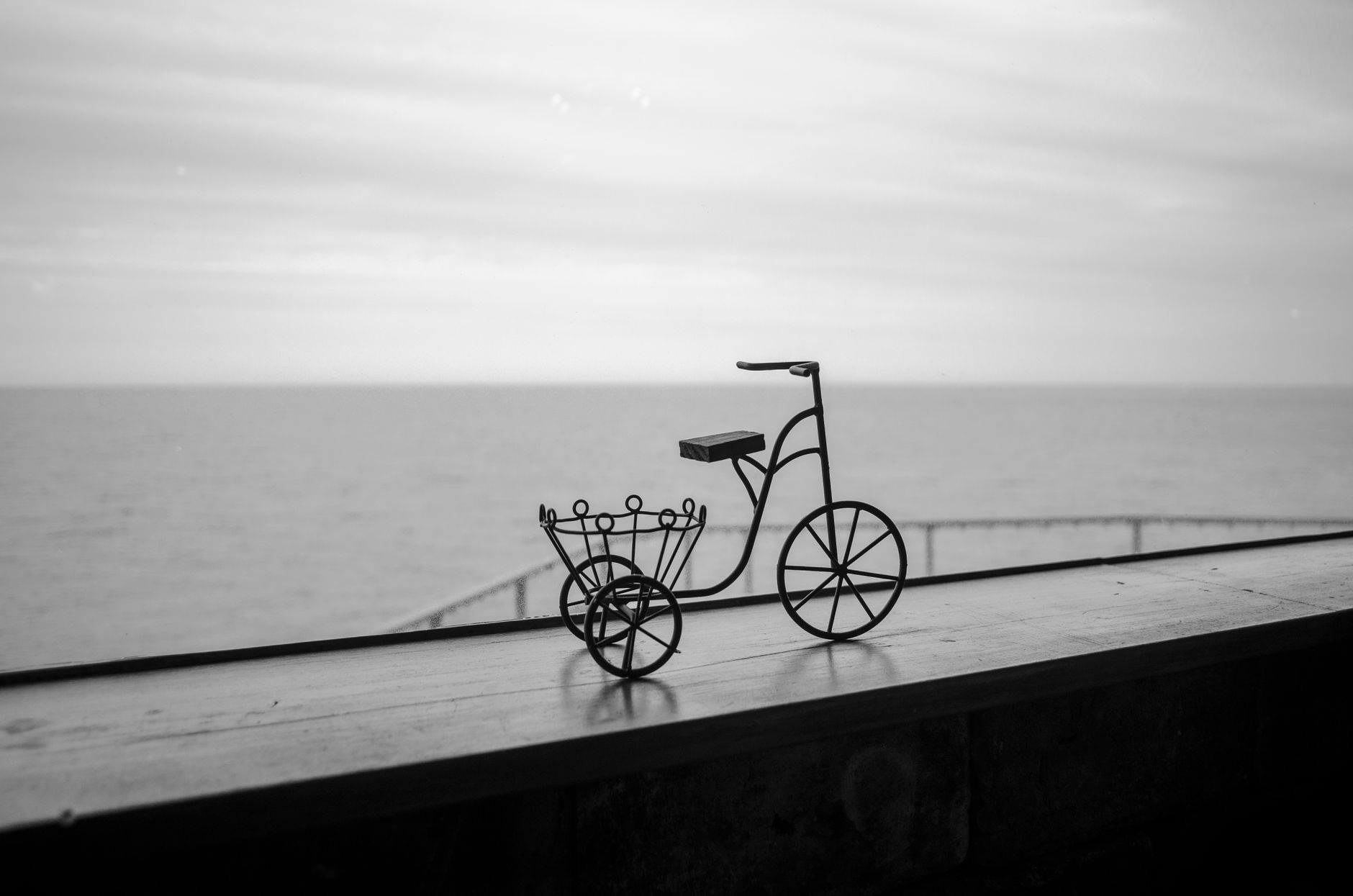 Scultura metallica di una bicicletta in equilibrio su un molo in riva al mare, in bianco e nero