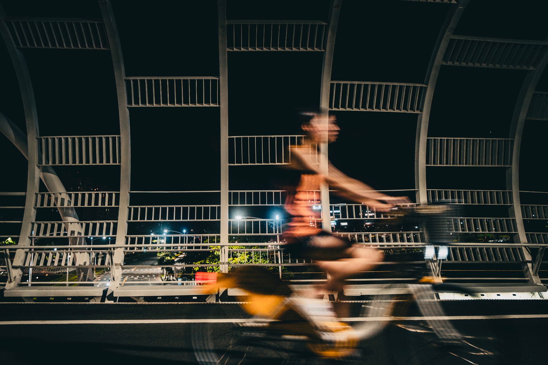 Ciclista sfocato in movimento su un ponte urbano di notte: la città che scorre